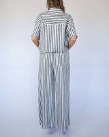 Back view of a woman wearing a relaxed, black and white striped cotton-viscose shirt and matching wide-leg pants.