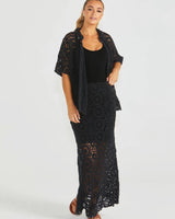 Model wearing a black Clover lace maxi skirt with an elastic waistband, styled with a matching lace top and black tank.