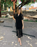 Woman wearing a black midi-length Clover lace skirt with a matching lace button-down shirt in a park setting.