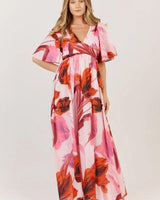 Pink cotton maxi dress featuring a bold floral print, V-neckline, wrap-tie waist, and soft gathered flutter sleeves.