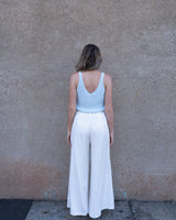 Woman wearing a pale blue sleeveless 100% cotton knit tank top with a V-neckline and white wide-leg linen trousers.