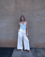 Woman wearing a pale blue textured cotton knit tank top with a v-neckline paired with white wide-leg trousers.