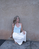 Pale blue cotton knit tank top with a v-neckline, sleeveless design, and straight hem worn with white trousers.