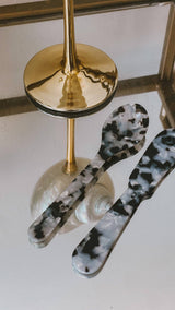 Saltist acrylic spoon and butter knife set in a black and white tortoiseshell pattern on a mirrored surface.