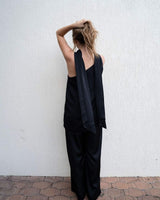 Woman wearing black wide-leg satin pants with a matching sleeveless top against a white wall.