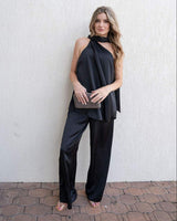 Woman wearing black satin wide-leg pants with a matching sleeveless halter top and a clutch bag.