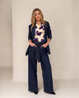 Woman wearing a dark denim Destiny blazer and matching wide-leg trousers with a floral top against a neutral background.