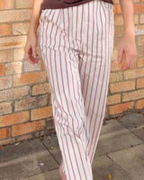 Straight-leg pants featuring vertical chocolate-brown stripes on a cream base with a secure zip and button fly.