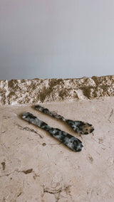 Saltist acrylic spoon and butter knife set in a grey and black tortoiseshell pattern on a stone surface.