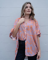 Woman wearing a loose-fit, mauve and orange island-print linen-blend button-up shirt, OSFA size.