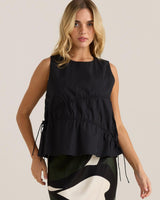 Black cotton sleeveless top with adjustable side ties and asymmetric gathering detail at the bust.