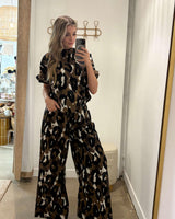 Woman wearing Ella wide-leg pants and matching top in a bold brown, black, and white leopard print.