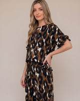 Woman wearing a brown, black, and white leopard print Ella reversible top with short sleeves and a high neckline.