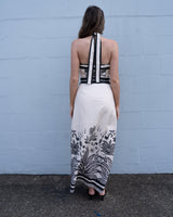Back view of a linen-blend maxi dress with a black and white halter neck, tie-back detail, and botanical print.