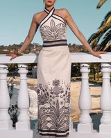 Beige linen-cotton maxi dress with a black halter neck, tropical leaf print, and form-fitting silhouette.