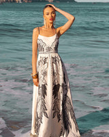 Woman wearing a white and black linen-blend Eloise sundress with adjustable straps and floral print on a beach.