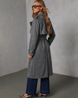 Woman wearing a charcoal grey suede trench coat with a belted waist, shoulder epaulets, and long sleeves.
