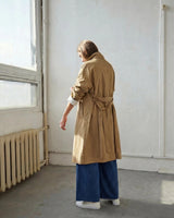 Woman wearing a relaxed-fit beige cotton nylon trench coat with a belted waist and cuffed sleeves over wide-leg blue jeans.