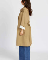Side view of a tan lightweight cotton-nylon trench coat with a relaxed fit, belted waist, and white cuffed sleeves.
