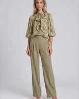 Model wearing a sheer olive plaid pussybow blouse with elasticated sleeves and tailored olive trousers.