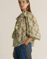 Green and beige plaid pussybow blouse with voluminous sleeves and a relaxed fit, paired with blue denim jeans.