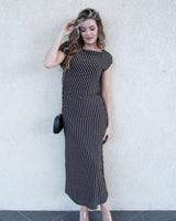 Woman wearing a black and gold metallic striped midi dress with a column silhouette and cap sleeves.