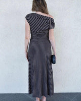 Woman wearing a black and metallic striped one-shoulder midi dress with a column silhouette.