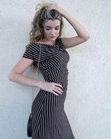 Woman wearing a one-shoulder metallic striped midi dress in a column silhouette against a textured wall.