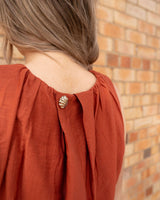 Rust-coloured Faith dress featuring a textured shell-shaped button detail and a structured, elegant silhouette.