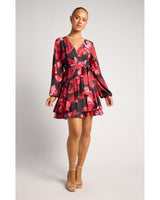 Model wearing a red and black floral print mini dress with a wrap-style V-neck, tie waist, and layered ruffle hem.