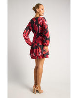 Model wearing a black and red floral print mini dress with long sleeves, tie waist, and a layered ruffle hem.