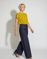 Model wearing a mustard yellow short-sleeved knit top with a round neck, paired with dark blue wide-leg denim jeans.