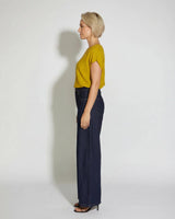 Woman wearing a mustard yellow short-sleeved knit top with dark wash wide-leg jeans against a white background.