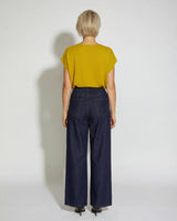 Back view of a woman wearing a mustard yellow short-sleeved knit top paired with dark wash wide-leg denim jeans.