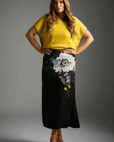 Model wearing a bright mustard yellow short-sleeved knit top paired with a black floral print midi skirt.