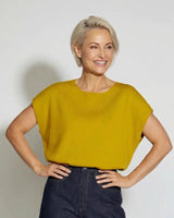 Woman wearing a mustard yellow, short-sleeved knit top with a round neckline and dark denim jeans.