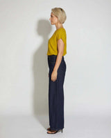 Woman wearing a mustard yellow short-sleeved knit top with dark wash wide-leg jeans against a white background.