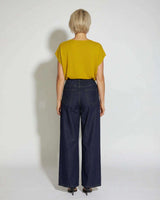 Back view of a woman wearing a mustard yellow short-sleeved knit top paired with dark wash wide-leg denim jeans.