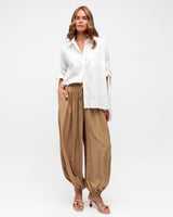 Model wearing caramel-colored Frankie balloon pants with an elastic waist and gathered cuffs, paired with a white shirt.