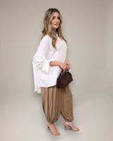 Woman wearing a white oversized cotton poplin shirt with gathered sleeve pull details and tan harem pants.