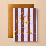 Christmas Greeting Card featuring red and pink vertical stripes with gold foil "Love & Hugs this Christmas" script and a matte antique gold envelope.