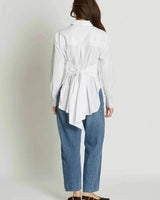 Woman wearing a white 100% cotton wrap-style shirt with an adjustable tie at the back, paired with blue jeans.