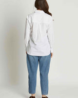 Back view of a woman wearing a crisp white 100% cotton button-down shirt with a collar and blue jeans.