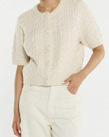 Cream cable knit short-sleeve cardigan with self-covered buttons and a ribbed crew neckline.