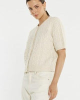 Cream cable knit cardigan with short sleeves, ribbed trim, and self-covered buttons worn by a model.