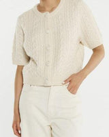Cream cable knit short-sleeve cardigan with self-covered buttons and a ribbed crew neckline.