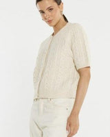 Cream cable knit cardigan with short sleeves, ribbed trim, and self-covered buttons worn by a model.