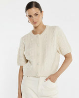 Cream cable knit short-sleeve cardigan with self-covered buttons and a ribbed crew neckline.