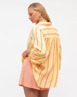 Woman wearing a yellow and orange striped cotton set with a relaxed-fit button-down shirt and matching shorts.