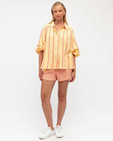 Woman wearing a yellow and orange striped cotton short set with balloon sleeves and a button-down shirt.
